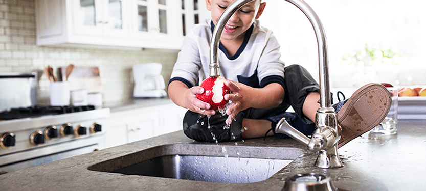 Boy rinsing an apple under a faucet with filtered water from a Culligan Water Filter